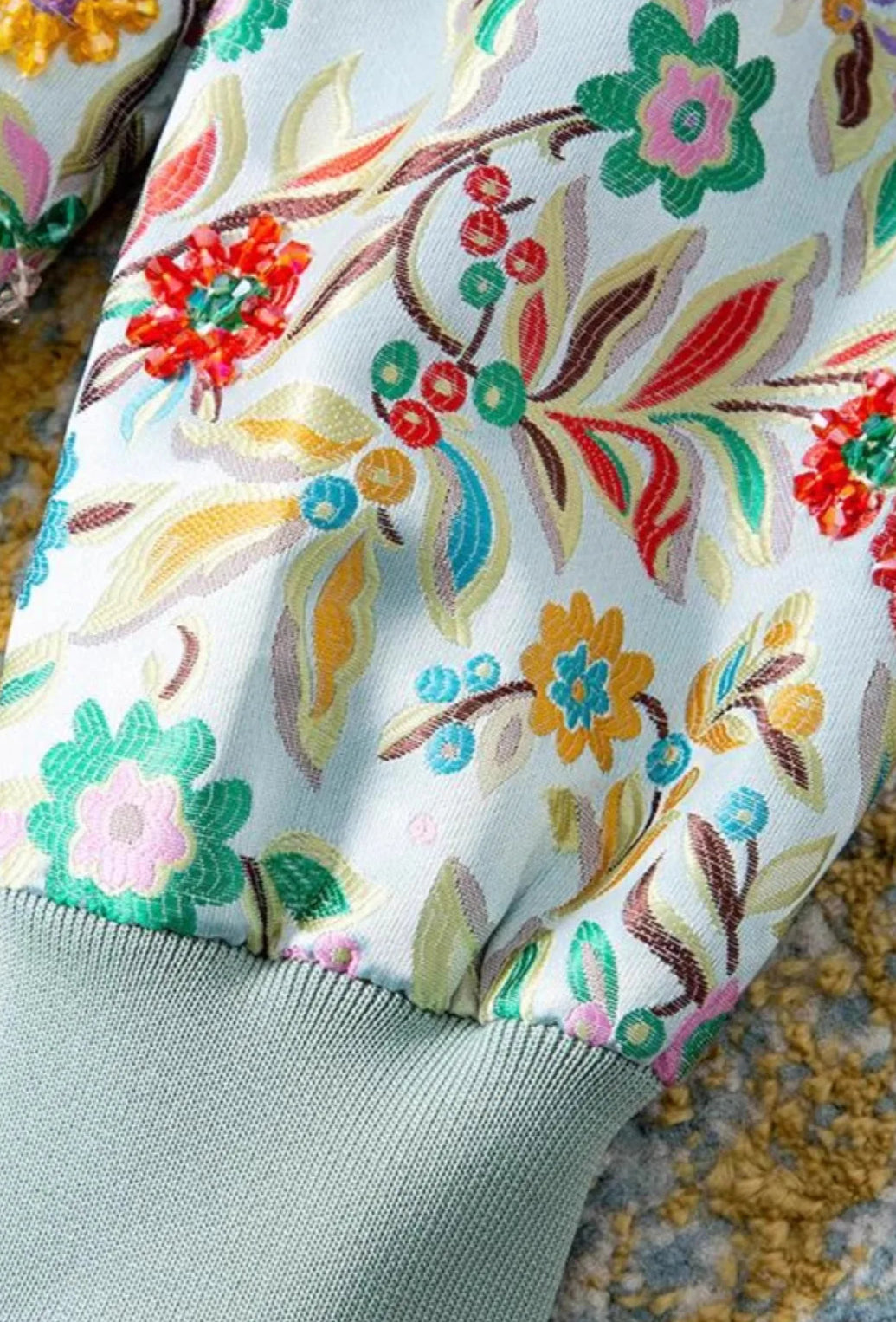 Close-up of floral embroidery on light blue bomber jacket sleeve, featuring colorful patterns and fine detailing | SuzzaneMarket