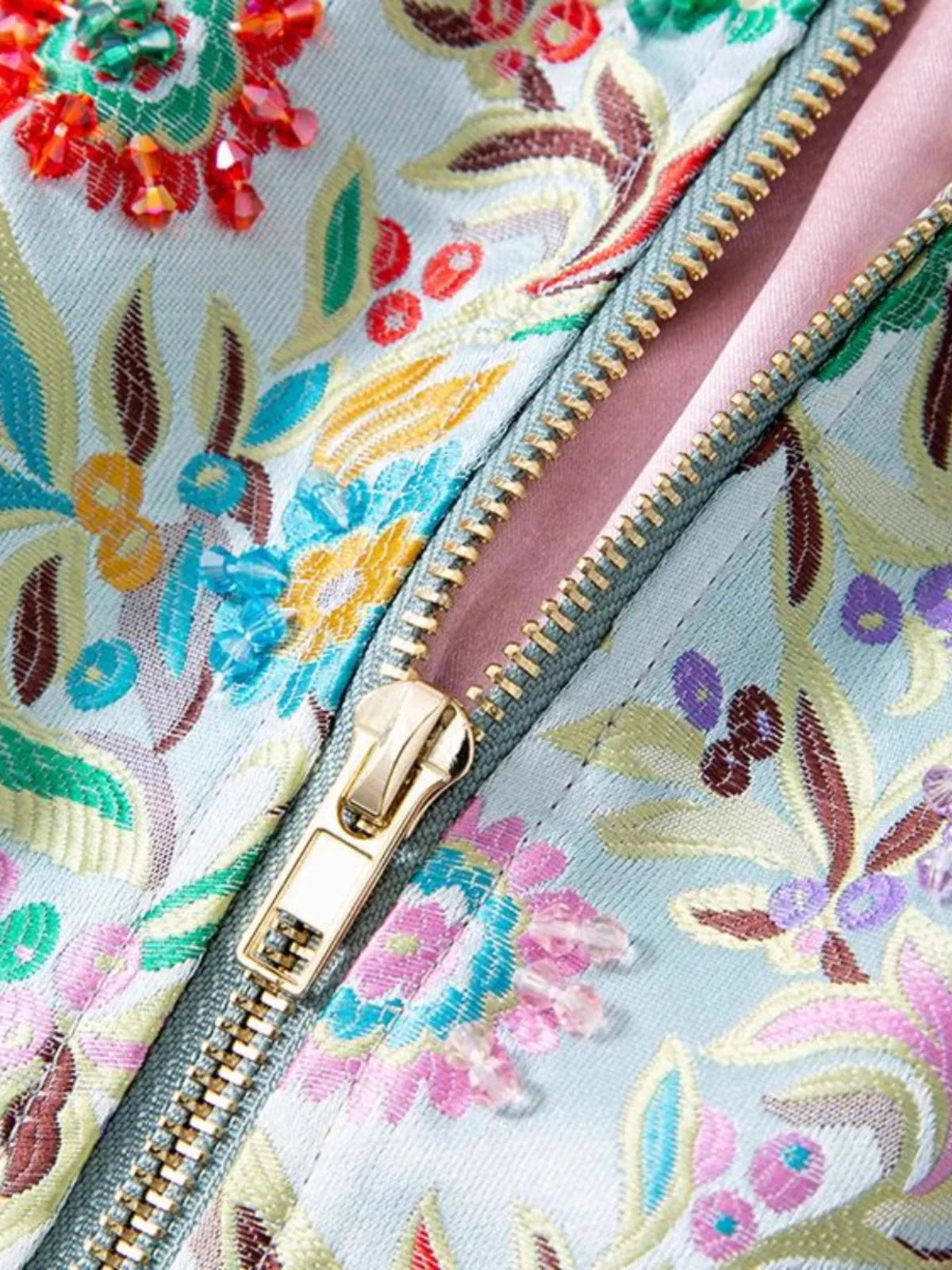 Close-up of colorful floral embroidery and zipper on bomber jacket in soft blue fabric | SuzzaneMarket