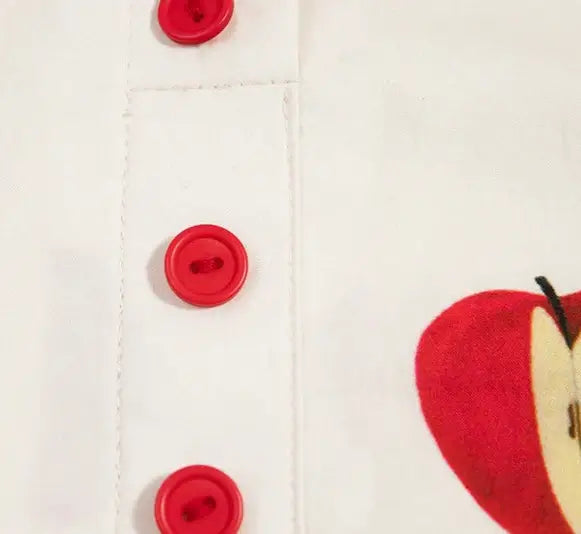 Close-up of red buttons on a white cotton dress with apple design | SuzzaneMarket.