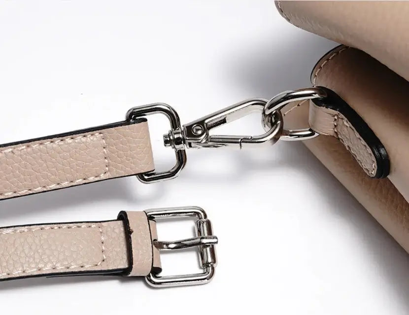 Close-up of the stylish beige tote bag strap with metal clips and adjustable buckle, showcasing premium leather quality.