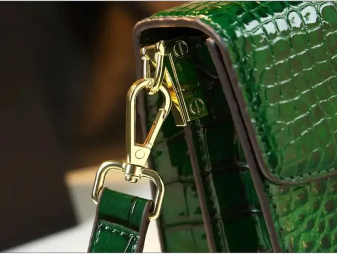 Close-up of green crocodile-embossed leather messenger bag clasp by SuzzaneMarket, showcasing gold hardware and classic design.