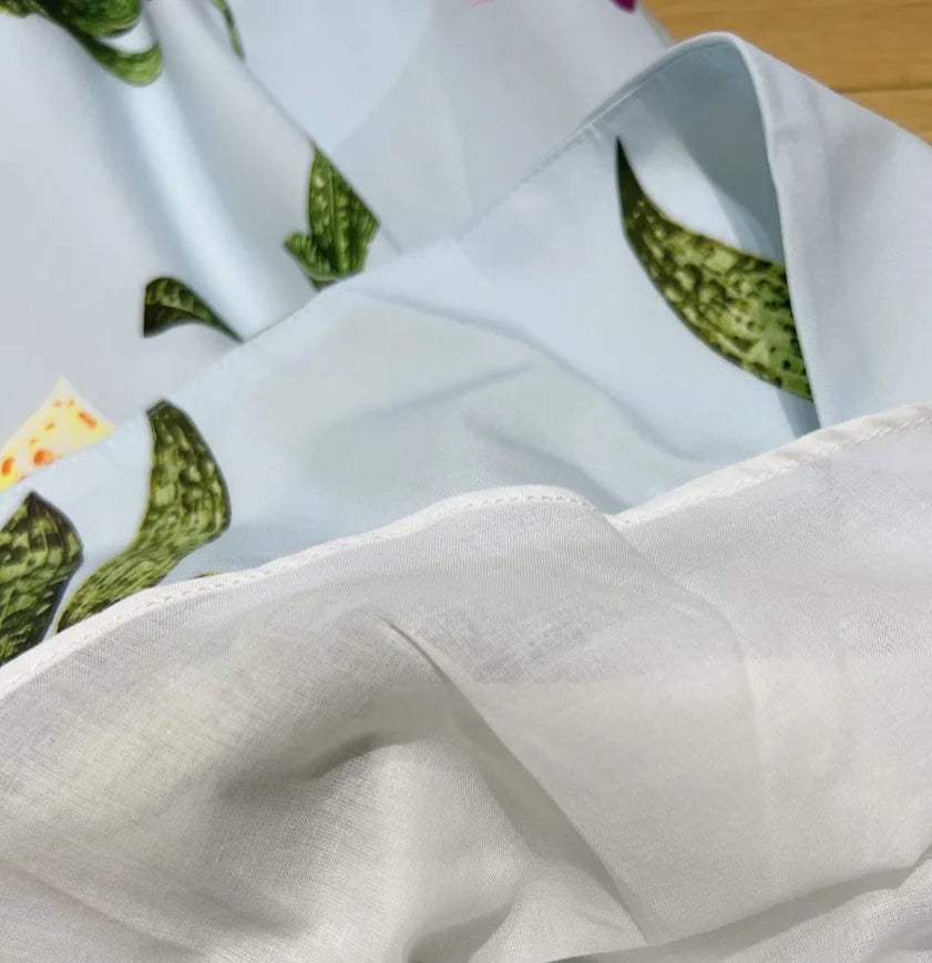 Close-up of a blue fabric with botanical prints and white lining, showcasing the texture and quality of the Robe Midi Popeline | SuzzaneMarket