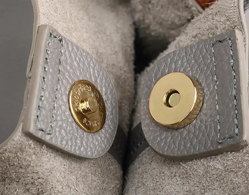 Close-up of textured gray leather with gold snap fasteners on a bag, highlighting high-quality craftsmanship.