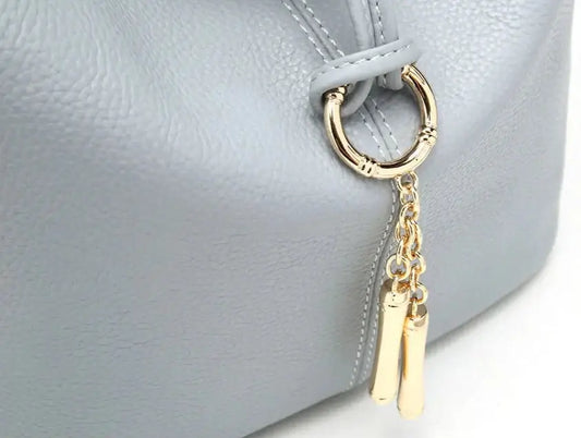 Detail of TILIS Hobo bag in light blue grained leather with decorative gold zipper and charm.